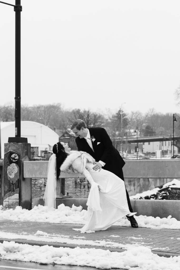A groom dips his bride along the snowy street outside The Bridge Lemont.