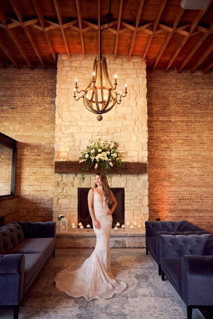 A bride poses for a photo in front of the Bridge Lemont fireplace.