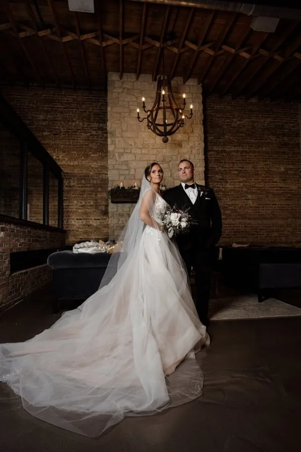 A bride and groom pose for a photo in front of the Bridge Lemont fireplace.