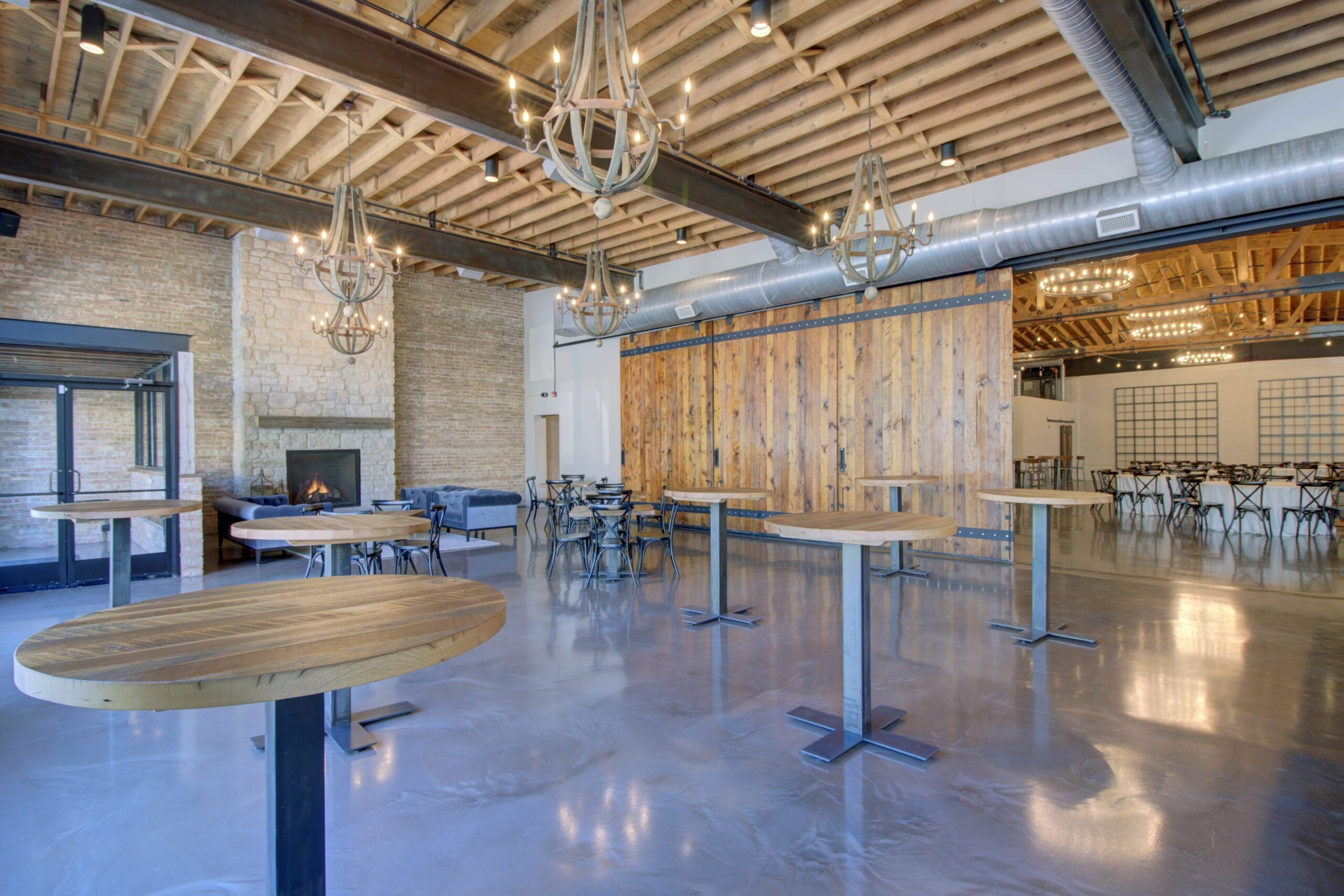 Open dining room with wooden chandeliers hanging from the ceiling and several standing cocktail tables.